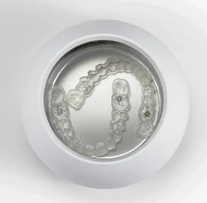 Clear aligner soaking inside an ultrasonic bath to demonstrate how to clean Invisalign retainers.