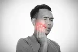 Close-up of a person holding their hand against their jaw with a pained expression, indicating a severe toothache.