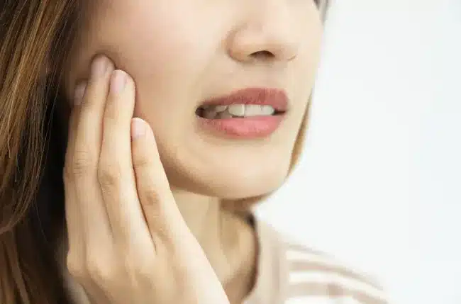 Close-up of a person gently pressing their fingers against their lower jaw, reflecting mild dental pain or discomfort.