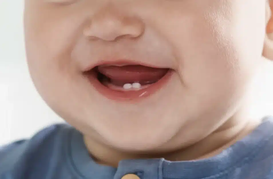 Close-up of a baby’s mouth showing two lower front teeth coming through.