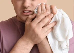 Man applying cold compress to jaw for recovery after wisdom teeth stitches